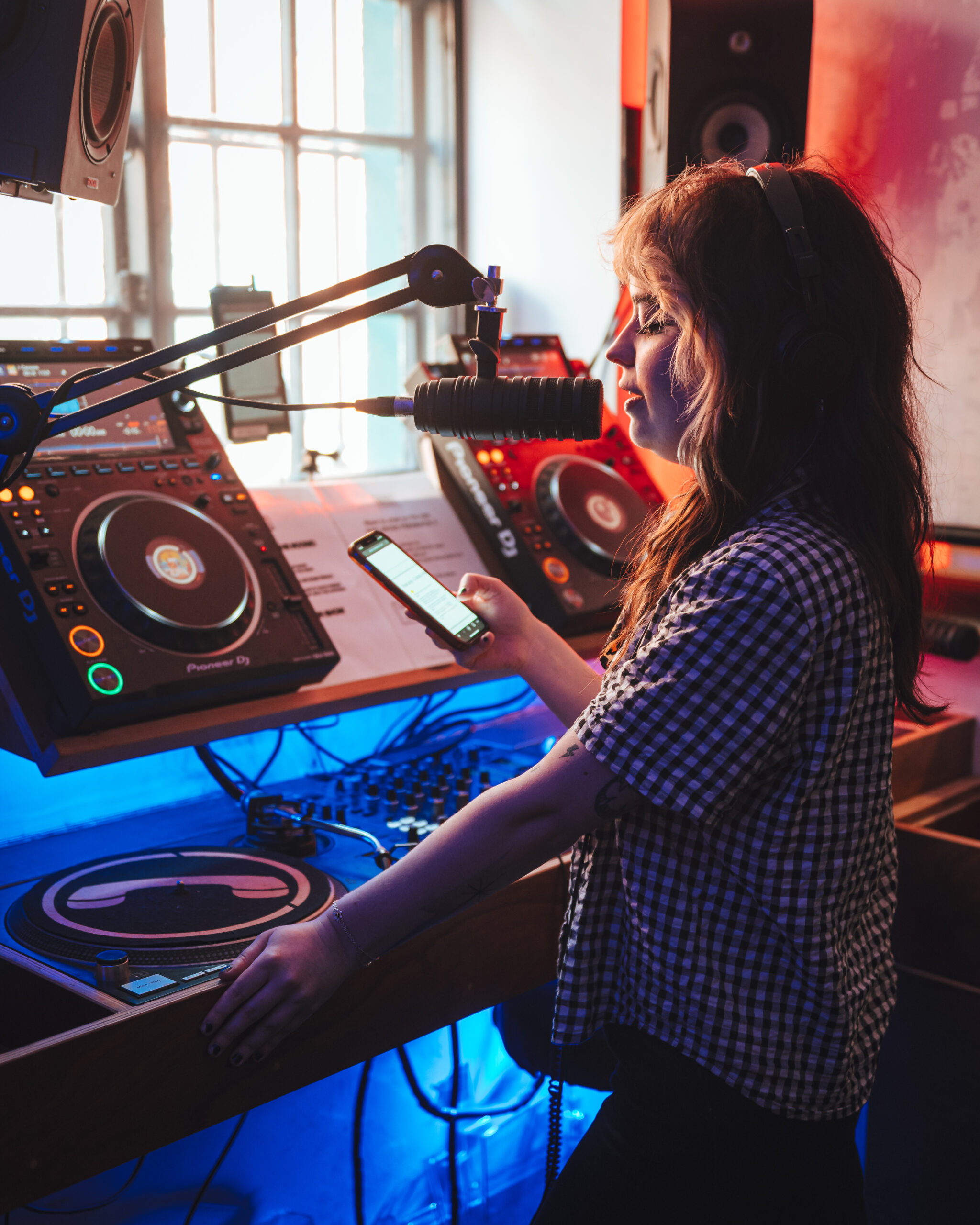 An image of a woman in front of DJ decks, speaking into a microphone.